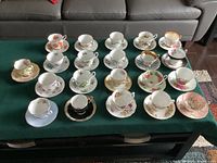 Full view of all 21 tea cups and saucers displayed on a green surface, arranged in rows.