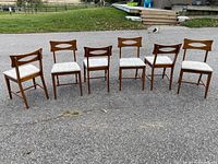 Six chairs side by side outdoors on pavement, showing full set