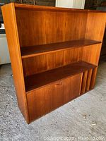 Full front and angled side view of the teak shelf unit showing two open shelves, a lower cabinet section, and vertical dividers.