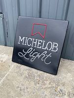Michelob Light beer neon sign photographed outdoors against a metallic blue-grey surface showing front face and flashes of neon colors.