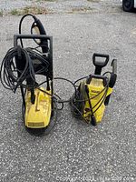 Photo showing two yellow Karcher power washers side by side outdoors with cords and spray guns coiled and attached.