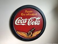 Front view of the 17 inch round wooden Coca-Cola sign featuring red background, yellow and white text, and a hand holding a bottle with wings detail.