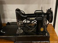 Side profile of black Singer 221 Featherweight sewing machine showing gold decals and top carry handle