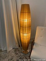Lit floor lamp showing full height and bamboo slatted shade with warm light.