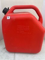 Front view of red jerry can showing flammability warning text embossed on surface.
