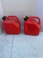 Two red plastic jerry cans side by side, both with black caps and integrated handles, placed on a white surface with plain background.