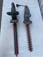 Two electric hedge cutters placed side by side showing their blades and handles on a white surface.