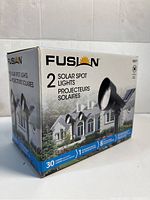 Box front and side views of Fusion branded solar spot lights packaging showing 2 pack and product features.