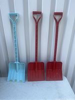 Three plastic shovels standing upright against a white background: one light blue and two red, showing overall shape and size.