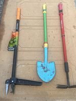 Three garden tools laid out horizontally on a flat surface: Fiskars hand tool, blue garden trowel, red cultivator fork