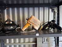 Three tools on shelf: Ozark Trail air pump, orange spray machine, black glue gun