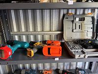 Four cordless drills placed on a metal shelf, three out of case, one in case with drill bits and accessories.