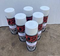 Photo showing six cans of J2 brand spray paint in black cans with white caps, labeled Super Gloss White.