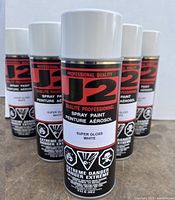 Front close-up view of J2 spray paint cans in super gloss white color showing labels.