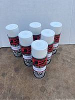 Six cans of J2 super gloss white spray paint arranged on a brown surface showing the front labeling and white caps.