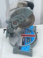 Side view of Delta miter saw showing blade, blade guard, base with angle markings, and adjustment lever.