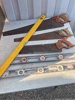 Three hand saws with wooden handles and rusted blades, placed alongside three spirit levels, one yellow wooden and two metal.