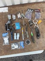 Complete view of assorted tools and hardware spread on wooden table, various hand tools, fasteners and clamps visible