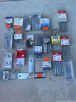 Overview of 21 packages of assorted hardware including screws, nails, anchors, brackets arranged on a surface.
