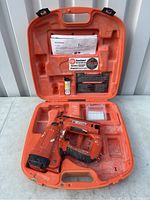 Open hard plastic orange case containing the Paslode finish nailer, user manuals, a bottle, and small accessory box