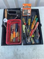 Top view of the open black plastic toolbox displaying the tools inside including screwdrivers, chisels, staple gun, and tape measure