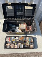 Top view of open black tool box showing contents of small screw packs in the main compartment and lid compartments.