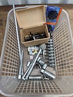 Tray containing metal socket wrench attachments, ratchet handle, extension bars, and beige container with hex keys and drill bits.