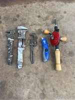 Full lot showing three pipe wrenches, red hand drill, blue utility knife, and small wrench on brown surface
