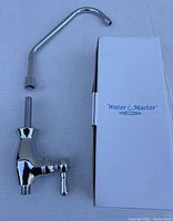 Photo of a chrome Water Master bar/kitchen faucet with a curved spout and single lever handle, placed beside its Water Master branded box on a white surface.