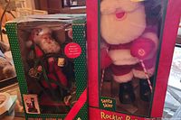 Photo showing two boxed Christmas Santa figurines, one on a sled and one plush Santa in a themed box.