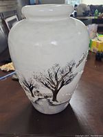 Straight view of white ceramic vase showing winter landscape with bare trees, houses, and snow details near bottom.