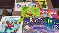 Photo showing collection of classic Walt Disney vinyl LPs including Pinocchio, Snow White, Peter Pan, Children's Riddles, Dumbo, Robin Hood, and Winnie the Pooh albums with colorful illustrated covers.