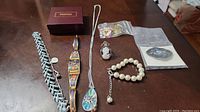 Photo of a collection of costume jewelry on a wooden surface showing bracelets, a necklace, rings, and brooches