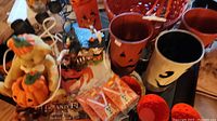 Photo showing a collection of Halloween themed items including candle holders, mugs, baskets and a lighted Halloween house figurine.