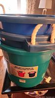 Three large plastic tubs stacked. Blue tubs on top and a green tub on bottom. Each tub has rope handles and thick plastic walls.