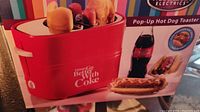Close-up photo of the red pop-up hot dog toaster featuring Coca-Cola logo and slogan, product designed to toast hotdogs and buns with pop-up feature.