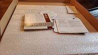 Box interior with the grill stone visible under foam padding, and accompanying manuals and instructions.
