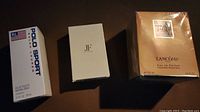 Front view of three sealed perfume boxes: Polo Sport, JF Femme, and Lancome Tresor