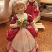 Front view of the Royal Doulton figurine showing the woman in red and white dress holding yellow flowers.