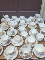 Photo showing a large assortment of over 30 tea cups and saucers, mostly decorated with pansy floral patterns in various colors and gold trim.