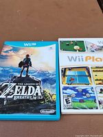 Photo shows two Wii U game cases; The Legend of Zelda Breath of the Wild in blue case and Wii Play sealed in white case.