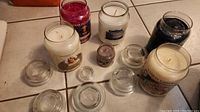 Photo of six Yankee Candles with glass lids removed and nearby, various scents visible, candles unburned.