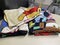 Three folded kids sofa blankets with character prints: Winnie the Pooh, Cars, and another cartoon.