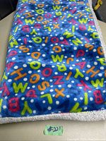 Blanket laid flat showing colorful alphabet print on blue background with some white polka dots and gray sherpa fleece border.