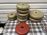 Weight plates stacked on table. Two smaller 2.5 lbs plates on left, stack of five 5 lbs plates in middle, two 10 lbs plates on right, one red 5 lbs Challenger plate in front.