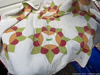 Full view of handmade quilt showing floral pattern in red, green, orange, yellow on white background
