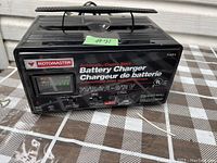 Black Motomaster battery charger with vents on the top and a carrying handle. Front panel shows model and power specifications. Minor age wear visible.