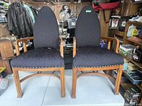 Front view of two matching Gothic Art Deco armchairs side by side on a white surface, showing wood frames and black upholstered seats and backs.