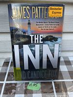 Front cover of the hardcover book 'The Inn' showing title, authors, lighthouse image, and bestseller sticker.