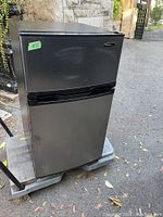 Front view of Danby stainless steel bar fridge with visible dent on door and age wear.
